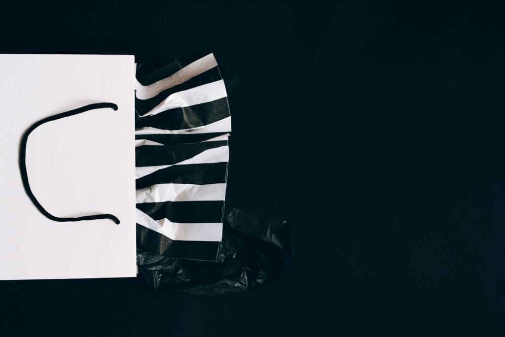 pexels-photo-5556278-5556278 White shopping bag with striped tissue paper on a black background, perfect for retail themes.