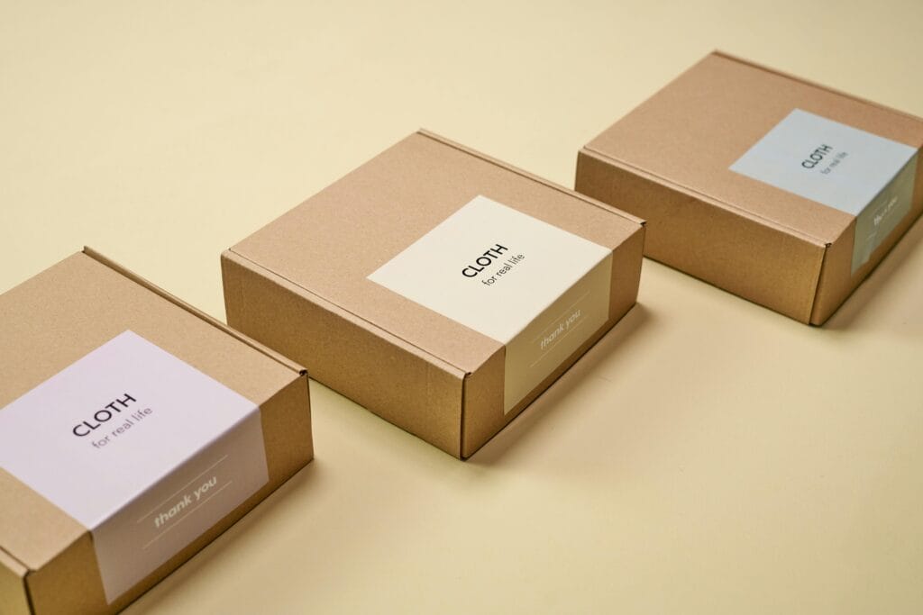 pexels-photo-9594428-9594428 Three minimalist cardboard packages labeled 'CLOTH' on a yellow background.